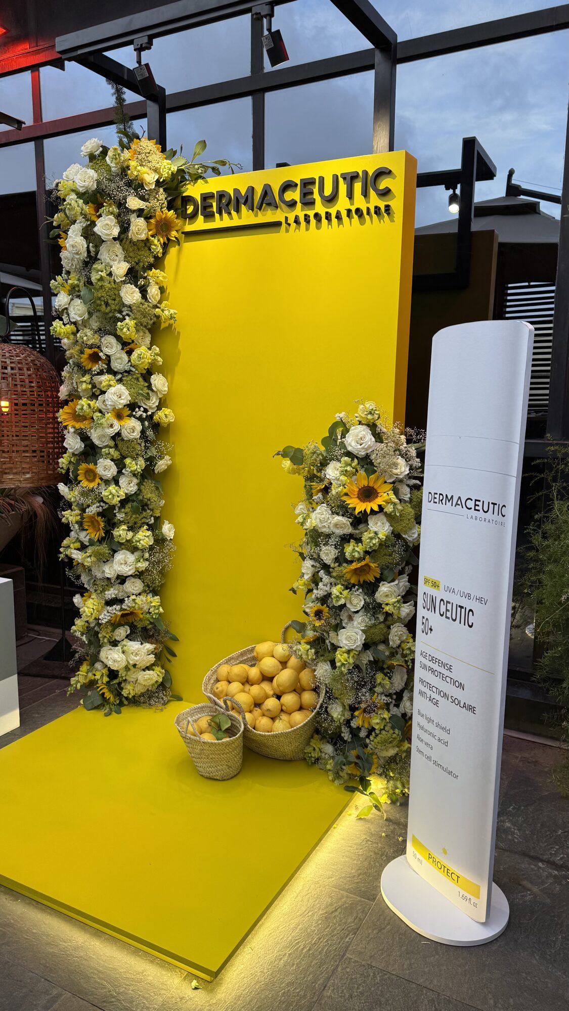 Dermaceutic product launch in Casablanca — yellow branded photo wall framed by white roses, sunflowers and lemon baskets, produced by SBAI Events Production