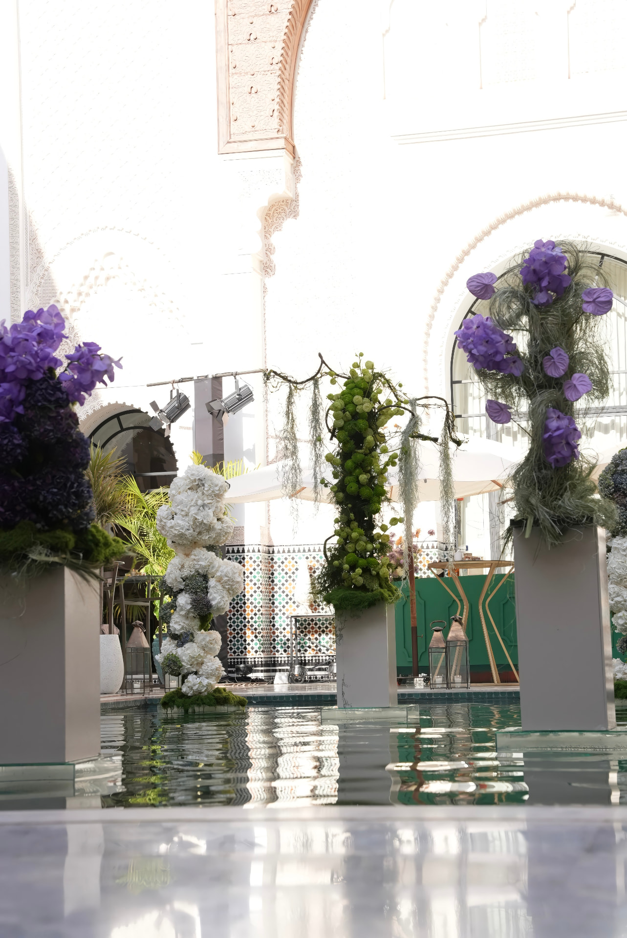 Gala Dinner Vegetal Garden at the patio of the Oberoi Marrakech — purple vanda orchids and anthuriums on white plinths above the emerald reflecting pool, ivory lounges and brass lanterns, produced by SBAI Events Production