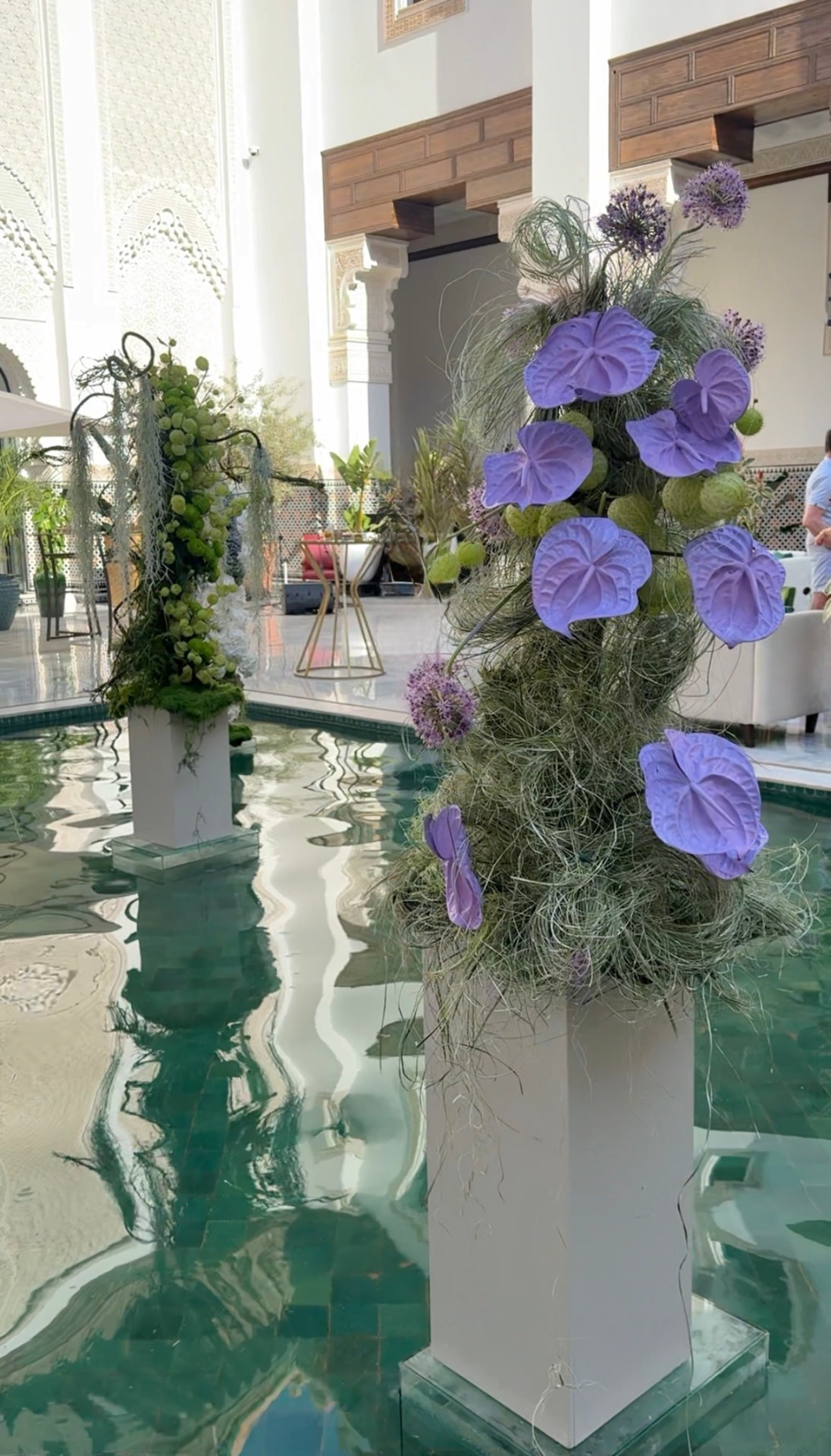 Gala Dinner Vegetal Garden at the patio of the Oberoi Marrakech — purple vanda orchids and anthuriums on white plinths above the emerald reflecting pool, ivory lounges and brass lanterns, produced by SBAI Events Production