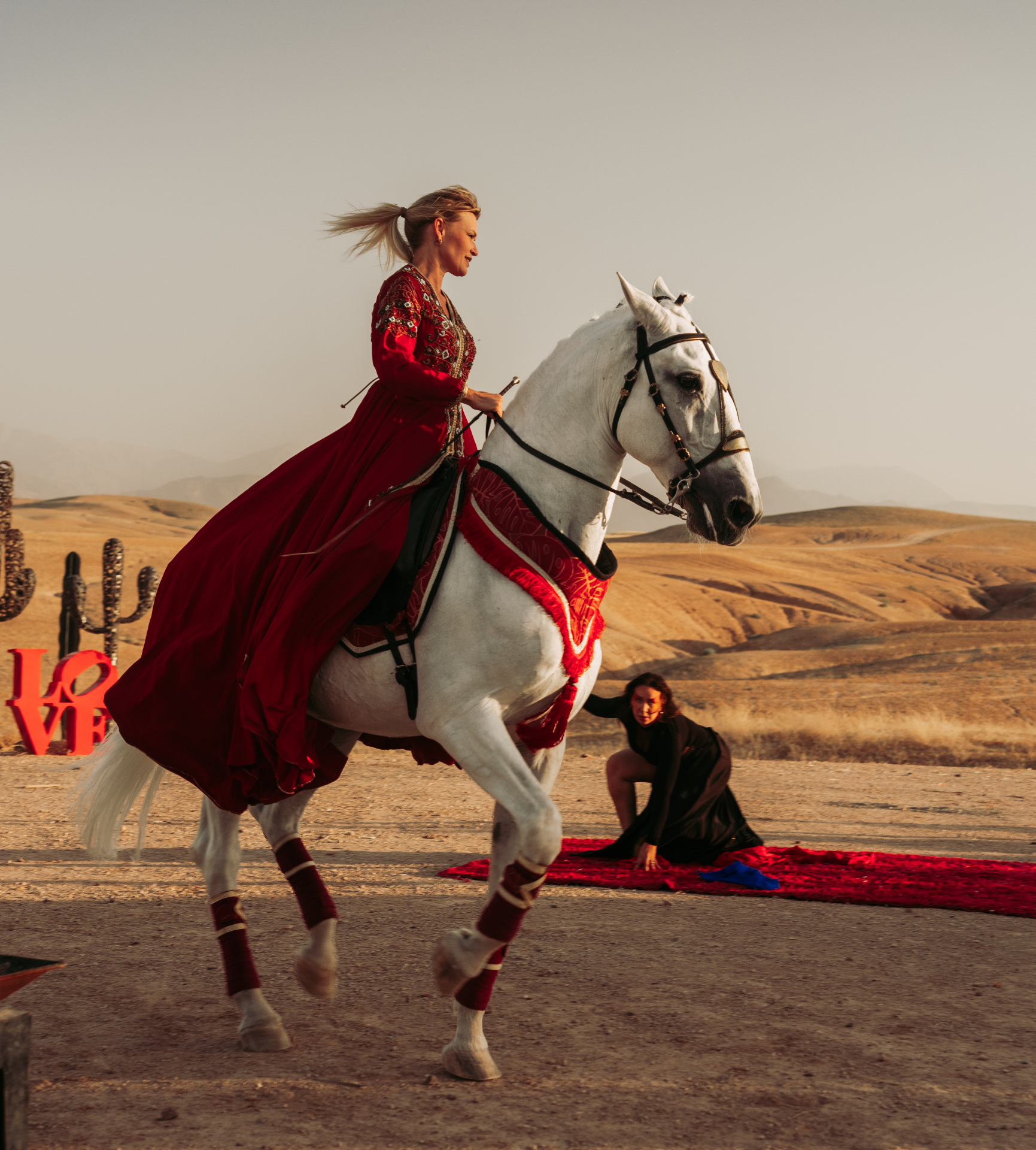Bride in a flowing red traditional gown riding a white horse across a golden desert landscape, styled by SBAI Events Production