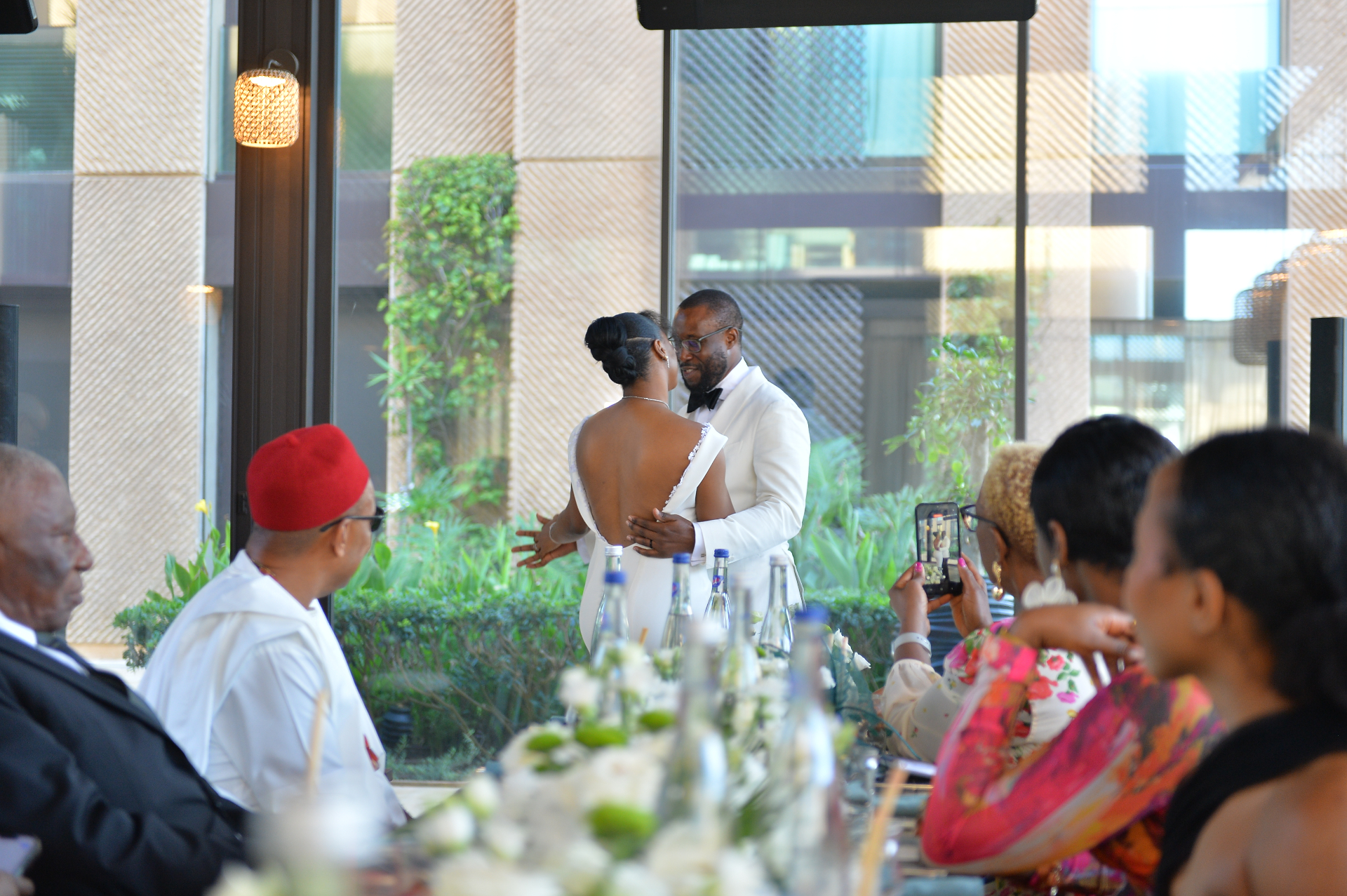 Bride and groom sharing an intimate moment at a sunlit wedding reception, surrounded by family and guests, captured by SBAI Events Production