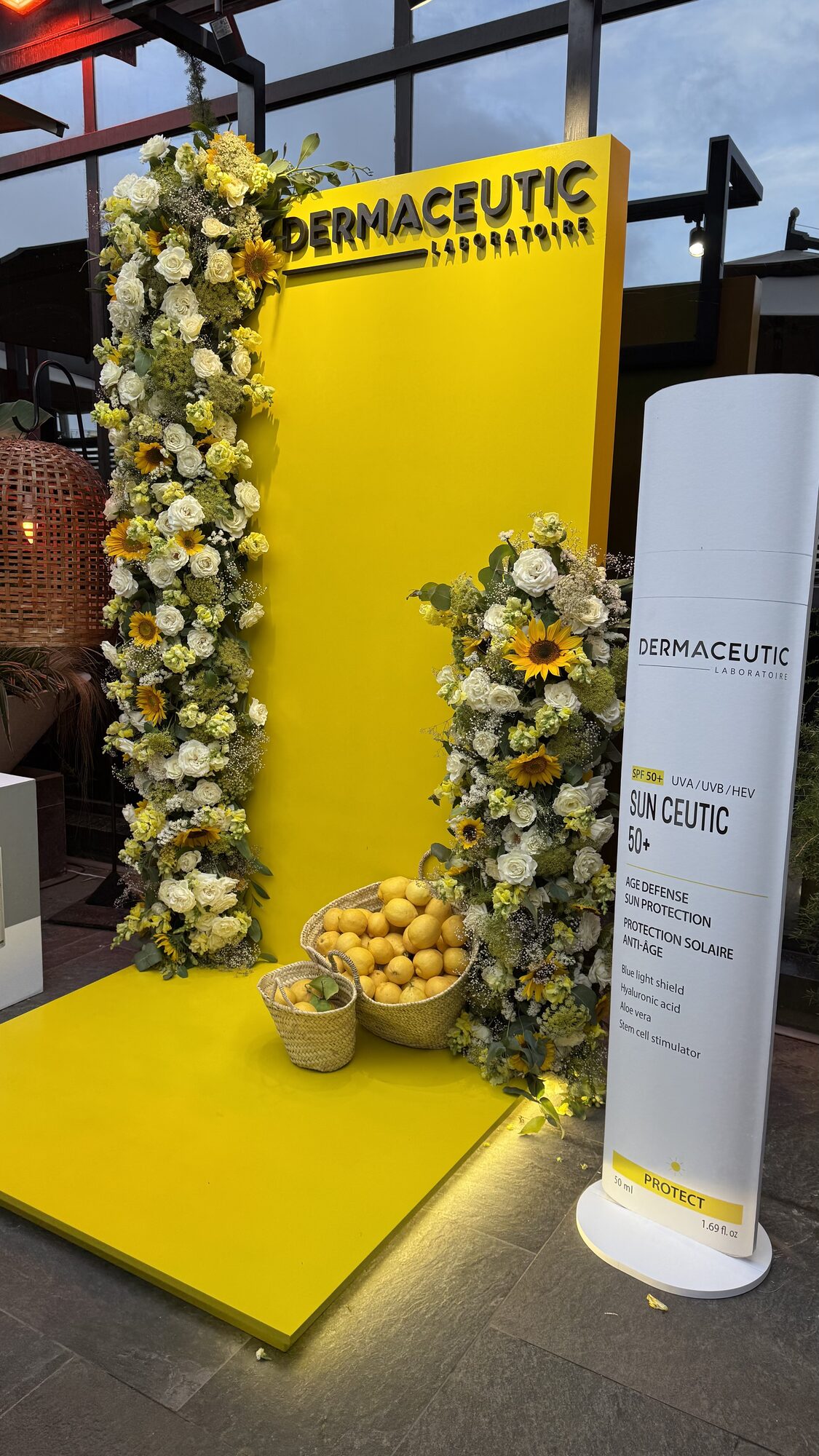 Dermaceutic product launch in Casablanca — yellow branded photo wall framed by white roses, sunflowers and lemon baskets, produced by SBAI Events Production