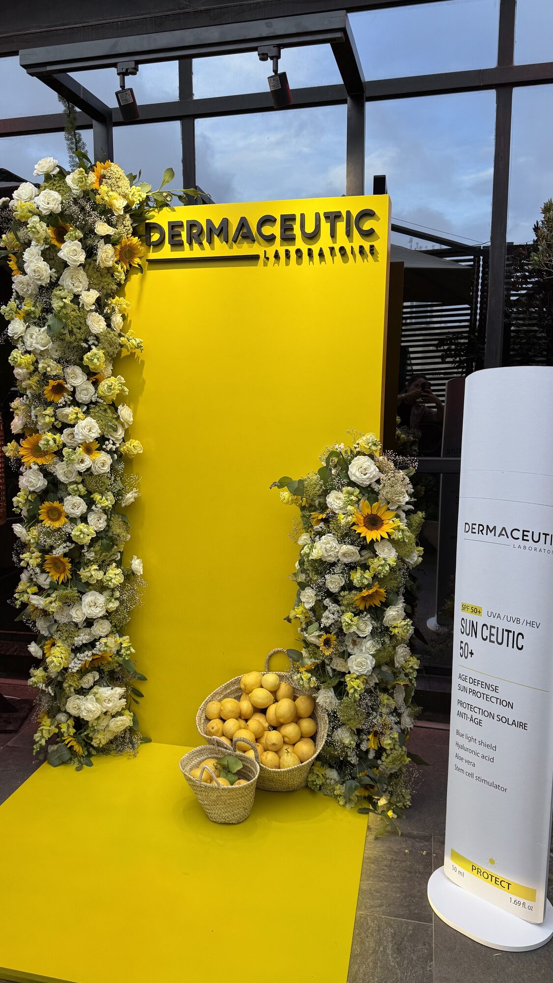 Dermaceutic product launch in Casablanca — yellow branded photo wall framed by white roses, sunflowers and lemon baskets, produced by SBAI Events Production