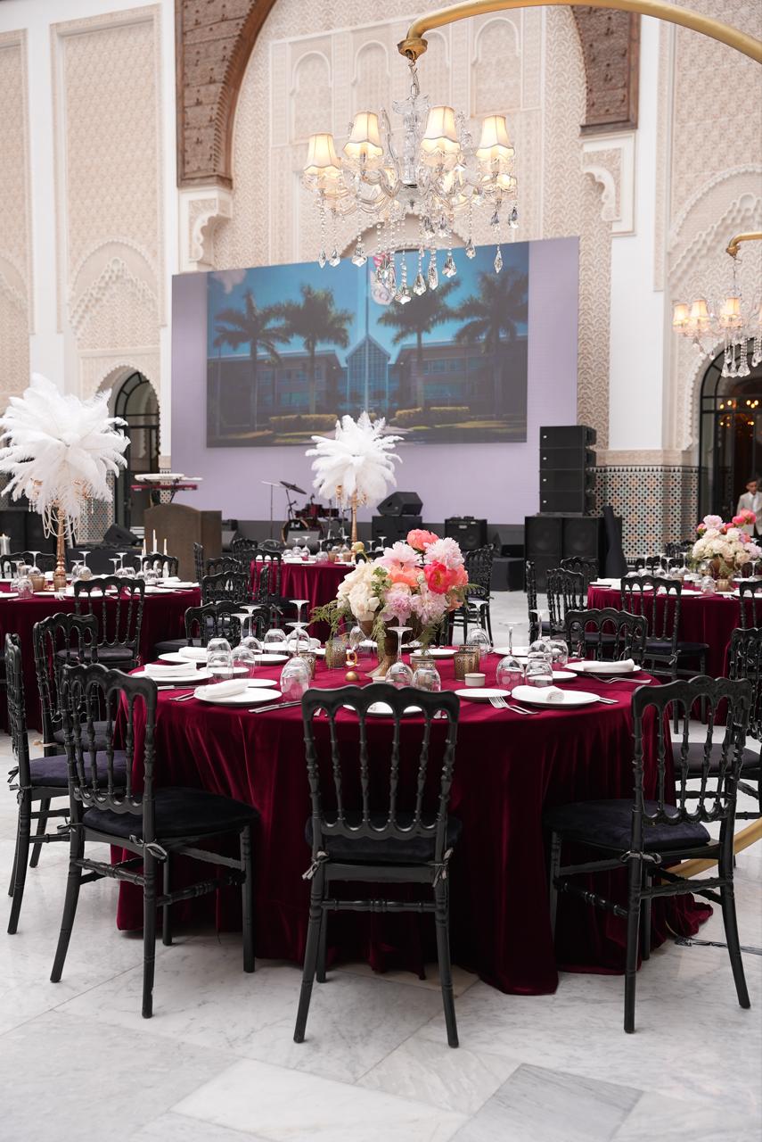 Burgundy banquet tables with white ostrich feather centerpieces set beneath a crystal chandelier and a Moorish arch, corporate gala produced by SBAI Events Production