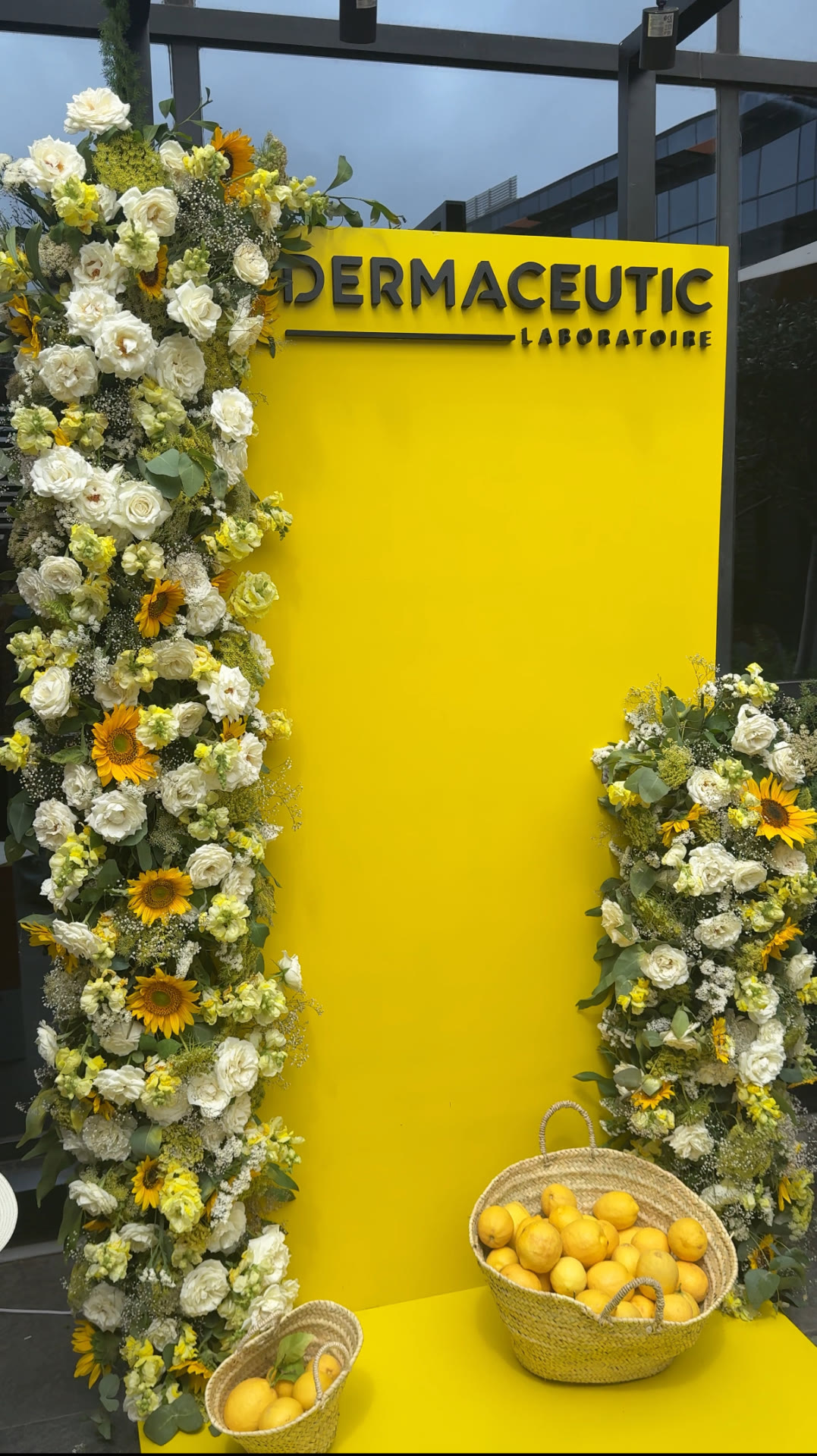 Dermaceutic product launch in Casablanca — yellow branded photo wall framed by white roses, sunflowers and lemon baskets, produced by SBAI Events Production