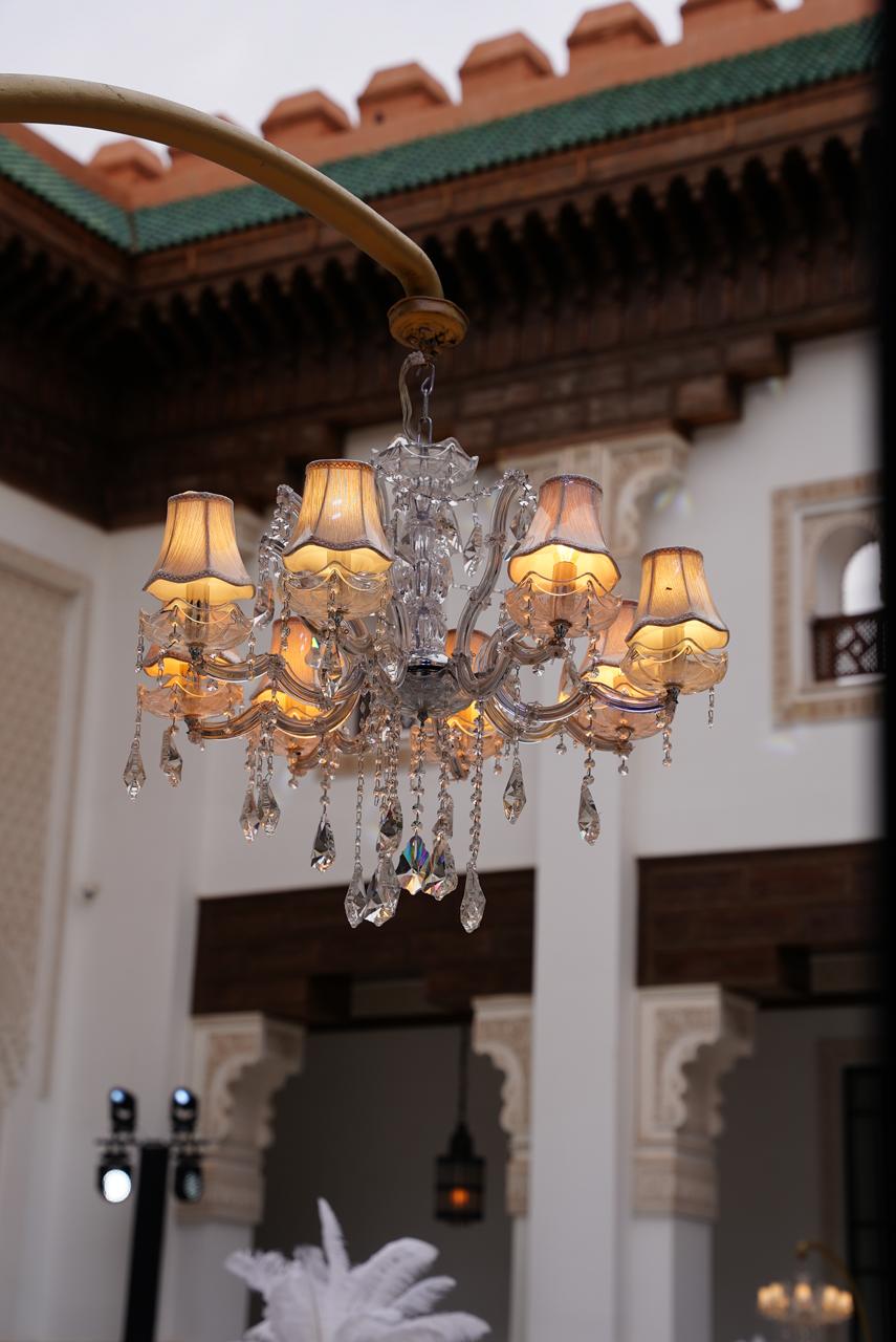 Antique crystal chandelier with silk shades hanging beneath a carved cedar-wood roof in a Marrakech riad, curated by SBAI Events Production