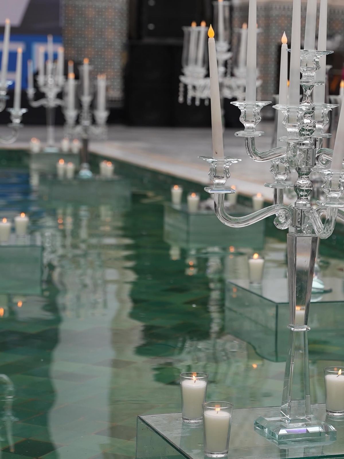 Close-up of crystal candelabras with lit taper candles installed on mirrored plinths in a candlelit reflecting pool, styled by SBAI Events Production