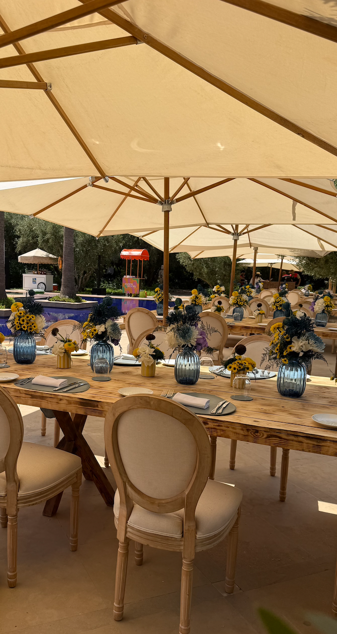 Pool Party in Marrakech — sunlit tablescapes, blue glassware and yellow floral centerpieces beneath ivory parasols, produced by SBAI Events Production